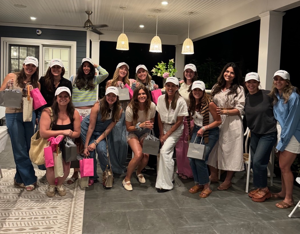 Moms in ai.moms™ hats holding pink gift bags at an ai.moms™ event